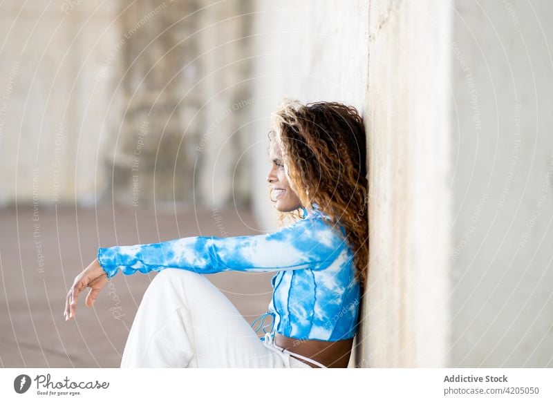 Stylish black woman sitting near building in city cool rebel outfit street style confident urban trendy female ethnic african american afro hairstyle curly hair