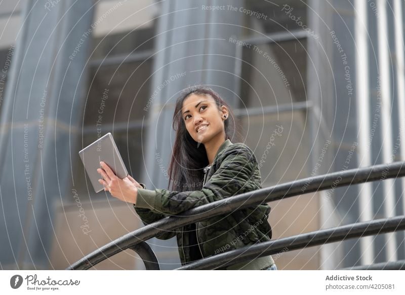 Asian woman using tablet on street lean railing urban casual smile modern female style asian young ethnic outfit browsing online surfing city gadget device