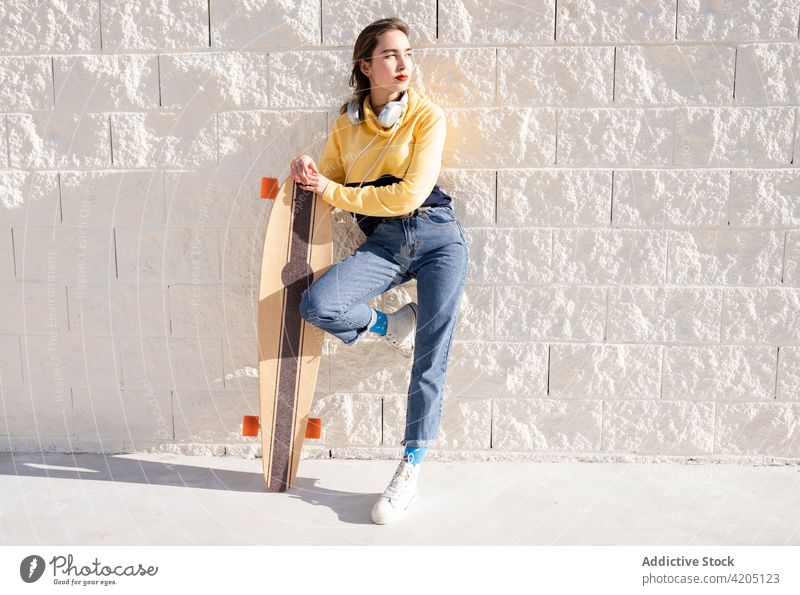 Stylish woman with longboard on pavement in sunlight skateboarder sport trendy cool wellness leg raised contemplate equipment wellbeing healthy lifestyle