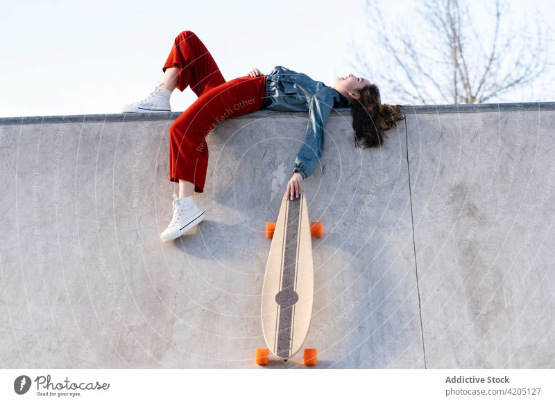 Skateboarder with longboard resting on skate ramp woman skateboarder sport tired exhausted sky skate park urban sportswoman stylish cloudy athlete trendy style