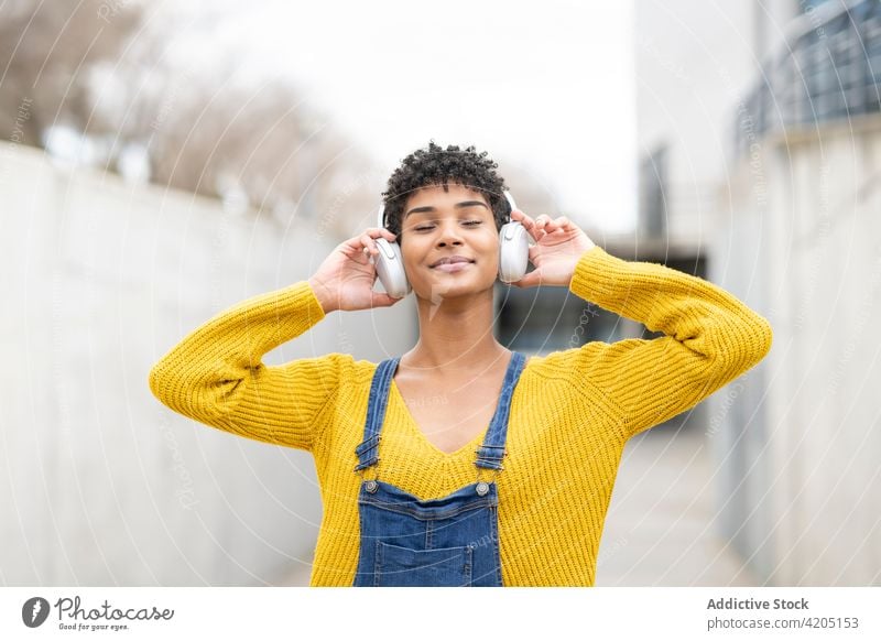 Happy black woman listening to music in headphones in city dreamy enjoy song wireless carefree female ethnic african american street pleasure eyes closed tune