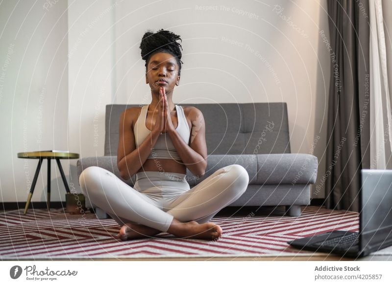 Barefooted black female meditating in Padmasana yoga pose with closed eyes woman padmasana lotus pose meditate eyes closed wellness zen laptop online wellbeing