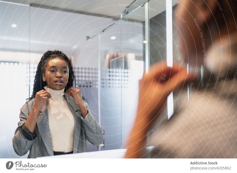 Positive young ethnic woman smiling while looking in mirror in bathroom smile self assured reflection style appearance charismatic happy joy female