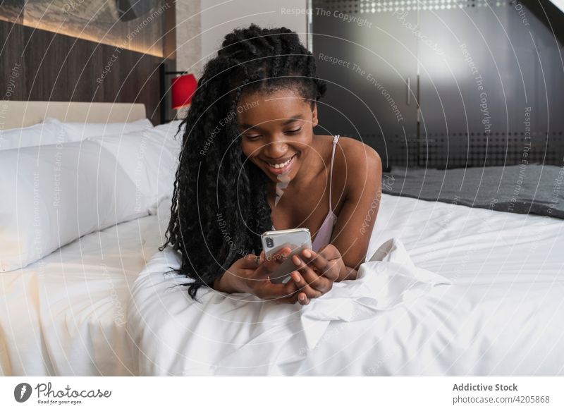 Cheerful young black lady using smartphone on cozy bed woman happy smile relax allure message social media online cheerful lying female african american ethnic