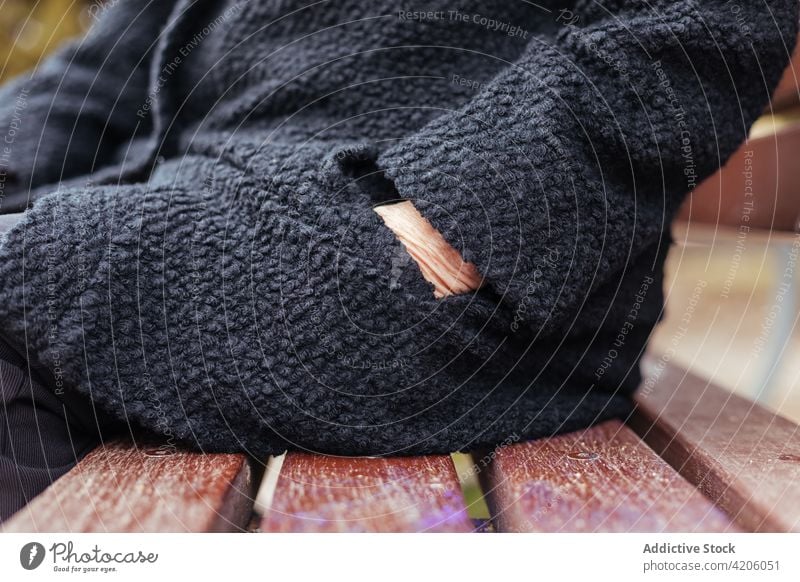 Side view of an anonymous elderly woman reaching into her coat pocket hand black faceless unrecognizable detail sitting winter resting crop 90s cold loneliness