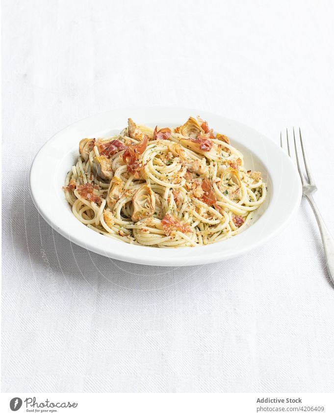 Closeup of a plate of spaghetti with artichokes seen from above food fresh tomato cheese pepper ham vegetable pasta prosciutto vegetarian dinner herb cream