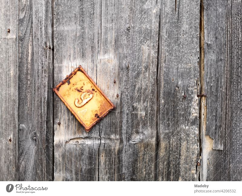 Dangling rusty tin sign with the house number on an old board wall in the old town of Alacati near Cesme at the Mediterranean Sea in the province of Izmir in Turkey.