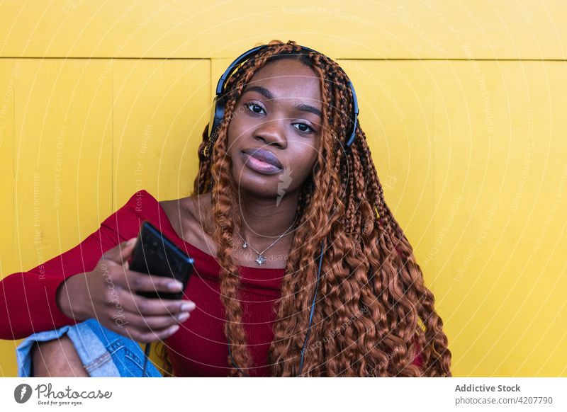 Black woman sitting listening to music near yellow doors in city doorway entrance building ancient street female ethnic black african american using wooden huge