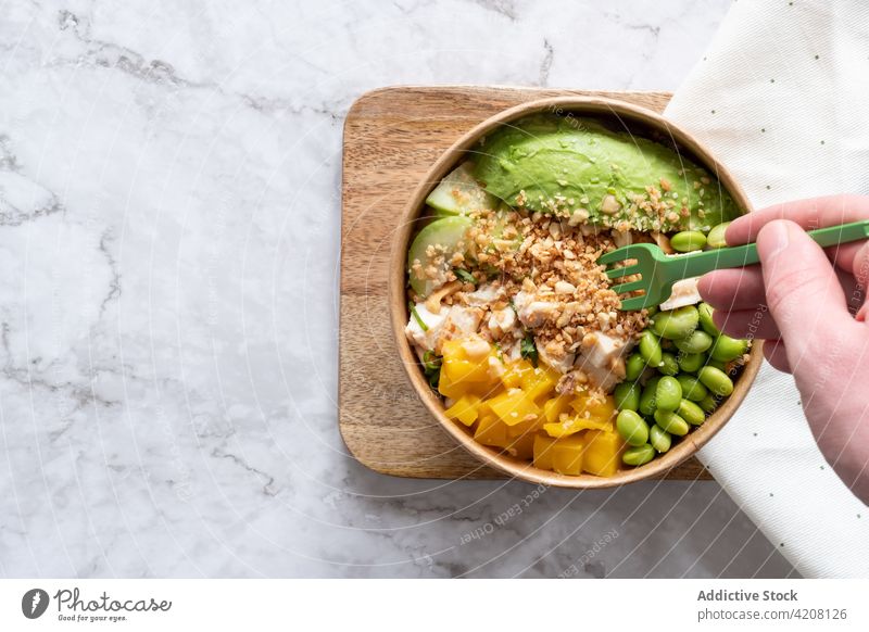 Crop person with bowl of tasty poke dish eat delicious assorted ingredient homemade serve wooden board cuisine table appetizing tradition delectable yummy meal