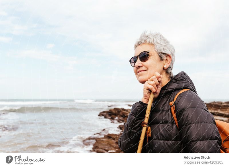 Content senior hiker admiring sea under cloudy sky admire ocean trek smile enjoy nature seascape woman portrait contemplate content pole trekker trip explore