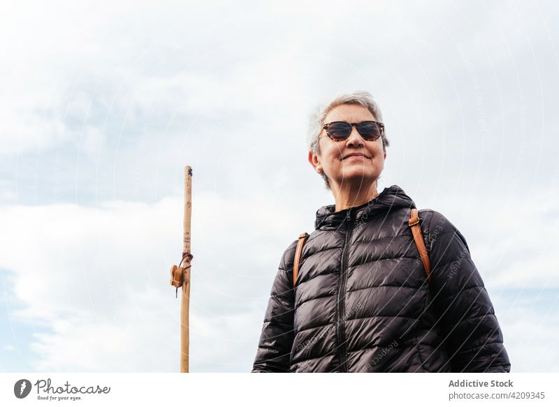 Content senior hiker admiring landscape under cloudy sky admire trek smile enjoy nature woman portrait contemplate content pole trekker trip explore wanderlust