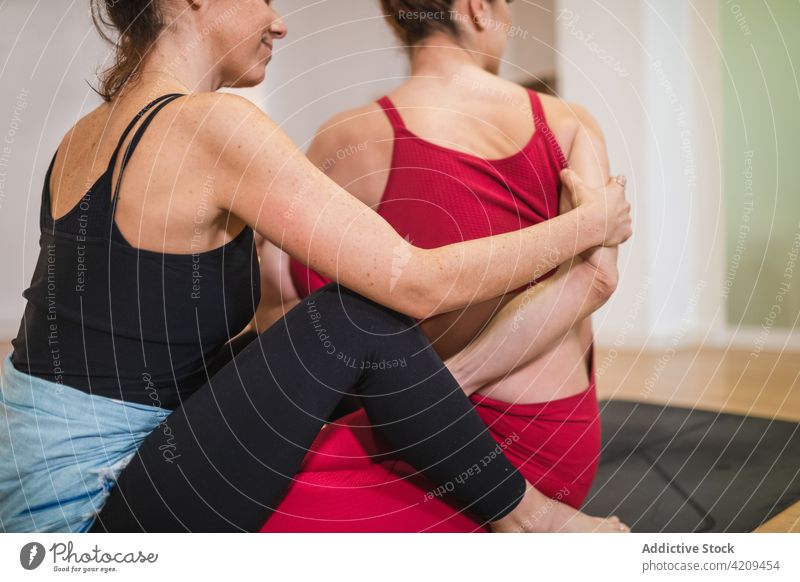 Trainer helping woman with stretching exercise women coach asana yoga twist wellbeing class position female practice together instructor support zen wellness