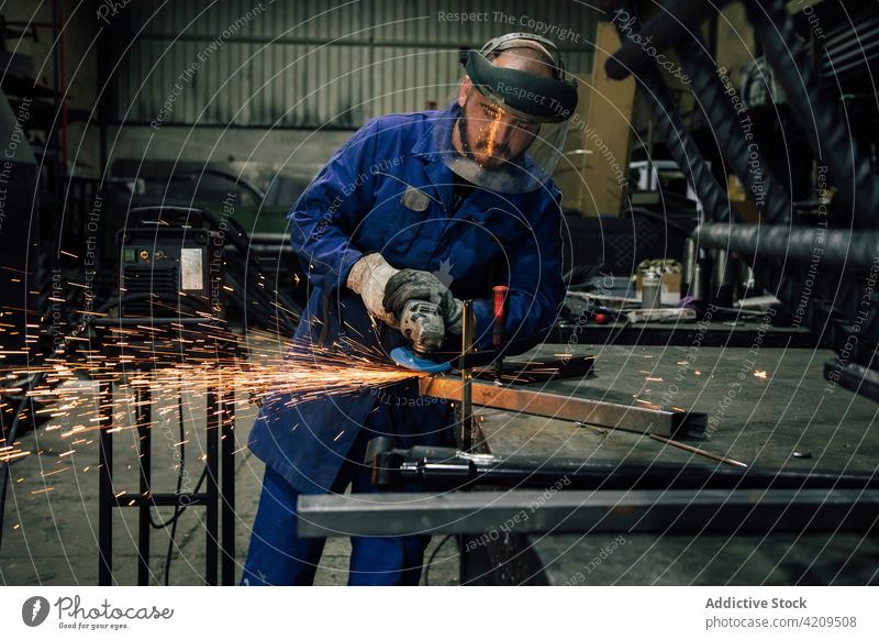 Man processing metal detail in workshop man welder angle grinder spark worker construction professional workwear mask equipment male light workspace workman