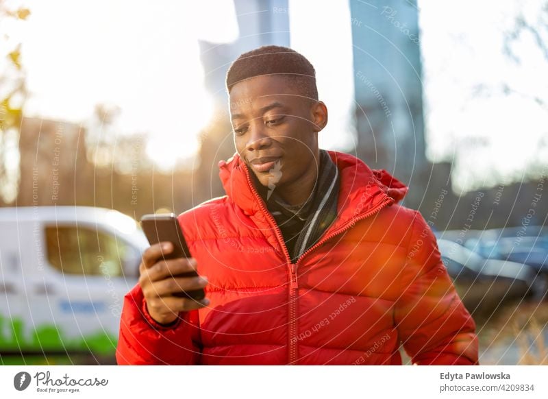 Young man using smart phone outdoors at urban setting black outside street millennial standing African city Warsaw real people casual lifestyle guy attractive