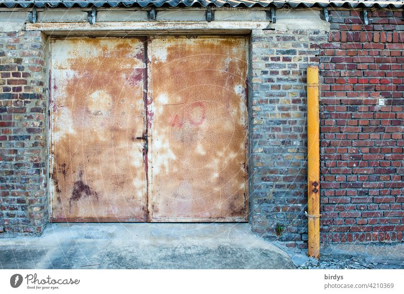 Old sheet metal gate on a warehouse with brick facade Goal Main gate steel gate Brick wall rusty Unkempt Warehouse Closed Downspout Front door