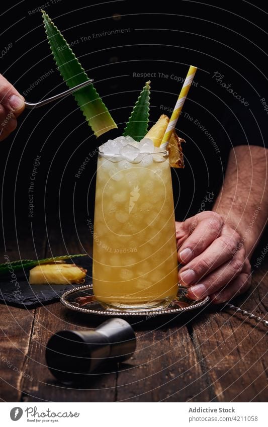 Faceless bartender decorating cocktail glass with pineapple leaves garnish cube straw tray table male leaf restaurant man decoration barman booze yummy bright