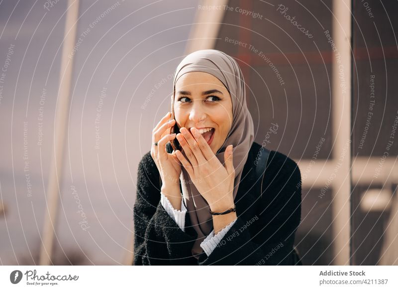 Cheerful Muslim woman speaking on smartphone in city talk hijab smile conversation phone call street female ethnic muslim mobile happy gadget glad content