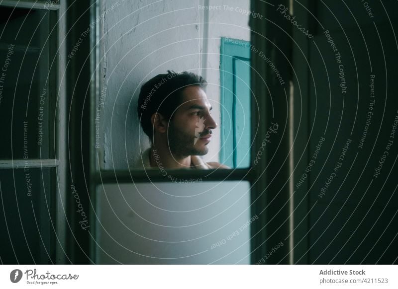 Peaceful man with naked torso standing at home and looking away peaceful shabby calm wall beard appearance shirtless male tranquil thoughtful individuality