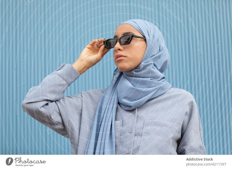 Trendy Muslim woman in sunglasses on blue background fashion style headscarf contemplate individuality accessory islam portrait casual cool modern color dreamy