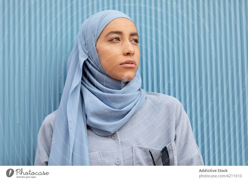 Dreamy ethnic woman in headscarf on blue background melancholy wistful lonely sincere contemplate pensive islam portrait style casual modern color thoughtful