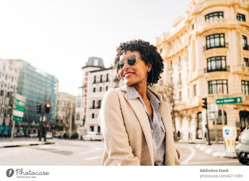 Cheerful black woman in trendy sunglasses smiling on street cheerful town smile positive happy coat urban fashion outfit city female young glad appearance