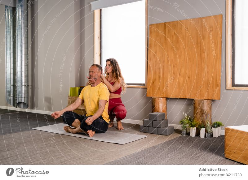 Calm man doing meditation while training in studio with instructor woman trainer session padmasana lotus pose concentrate practice focus female yoga sportswear