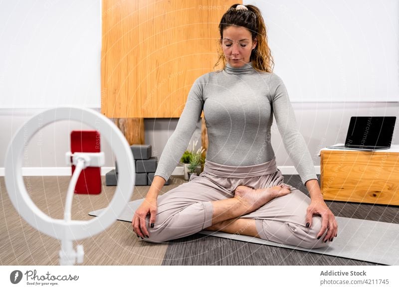 Woman meditating in Padmasana yoga pose woman padmasana lotus pose meditate vlog eyes closed smartphone tripod blogger practice female young activewear home