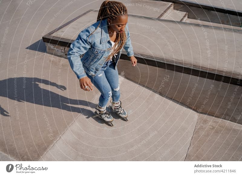 Ethnic woman rollerblading in skate park rollerblade ride move cool hobby summer style female ethnic black african american denim trendy braid ramp carefree