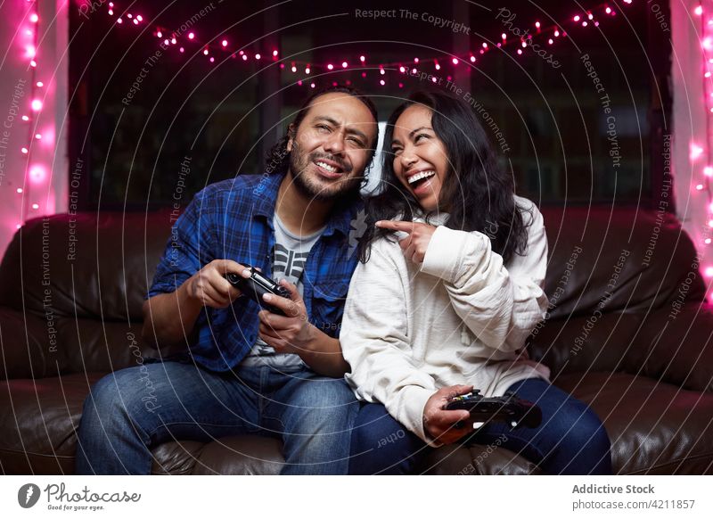 Delighted ethnic couple playing video game together delight videogame excited couch joy pad having fun entertain laugh gamepad free time device pastime