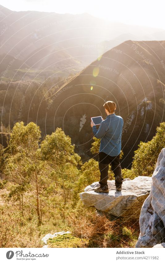 Traveler with tablet standing on rocky hill in highlands traveler mountain man admire enjoy viewpoint freedom male vacation explore nature scenery adventure