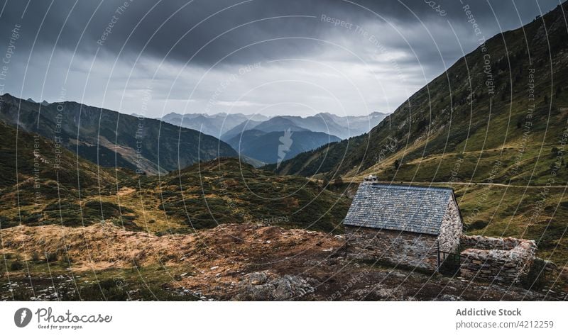 Small hut in grassy mountainous terrain in gloomy day highland valley aran field val d aran spain catalonia pyrenees nature cloudy sky landscape fence slope