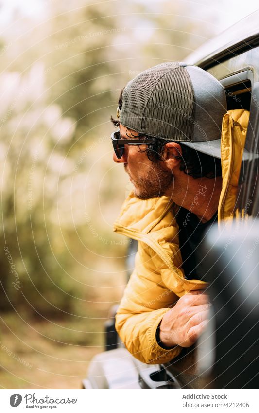 Adventurer in a cap and sunglasses peeking out of the car sale man window travel transportation road trip looking young face person journey portrait adult