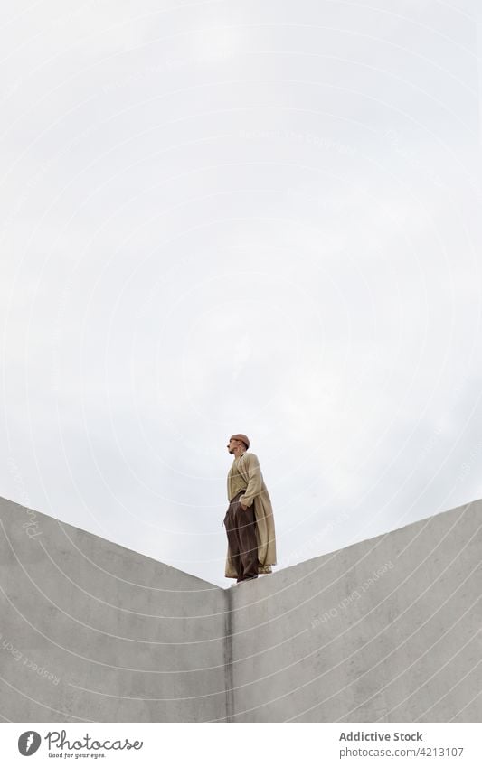 Man standing on edge of concrete wall man lonely gray sky solitude mood melancholy atmosphere male hand in pocket alone contemplate calm city corner building