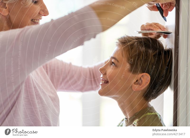 Mother measuring the height of her son against wall at home growth family mother happy smiling people child boy kid kids children lifestyle offspring house