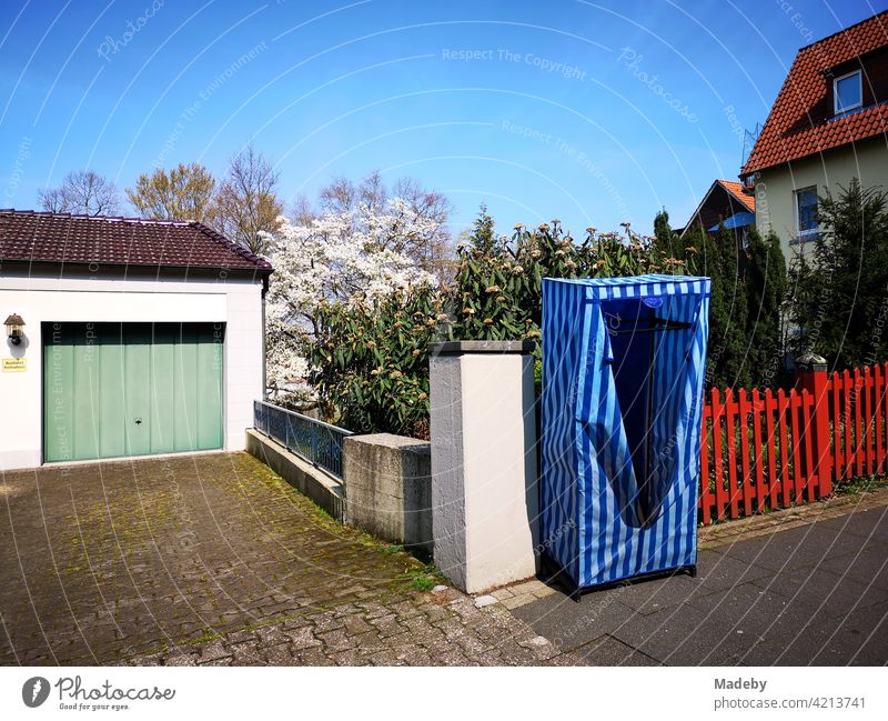 Mobiler blauer Kleiderschrank mit Streifen und Reißverschluss vor rotem Zaun auf dem Bürgersteig in Oerlinghausen bei Bielefeld am Hermannsweg im Teutoburger Wald in Ostwestfalen-Lippe