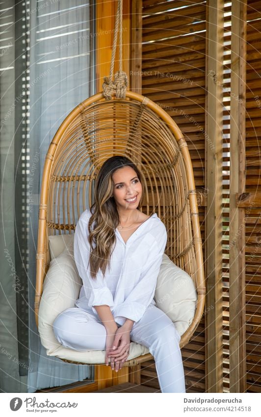 Cheerful woman resting in wicker hanging chair chill natural wooden happy style enjoy furniture rattan cushion comfort home smile cheerful design charming