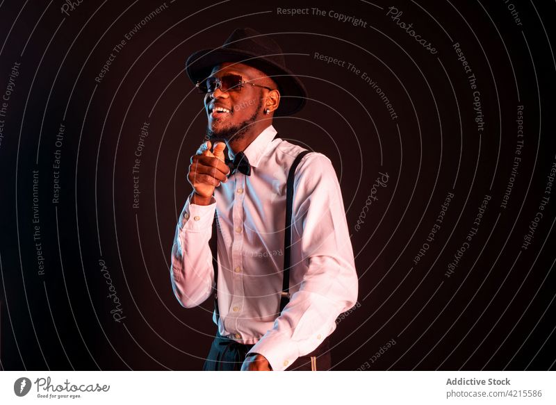 Stylish black man in white shirt and hat dancing on black background model style fashion well dressed gentleman dance tiptoe masculine portrait macho sunglasses