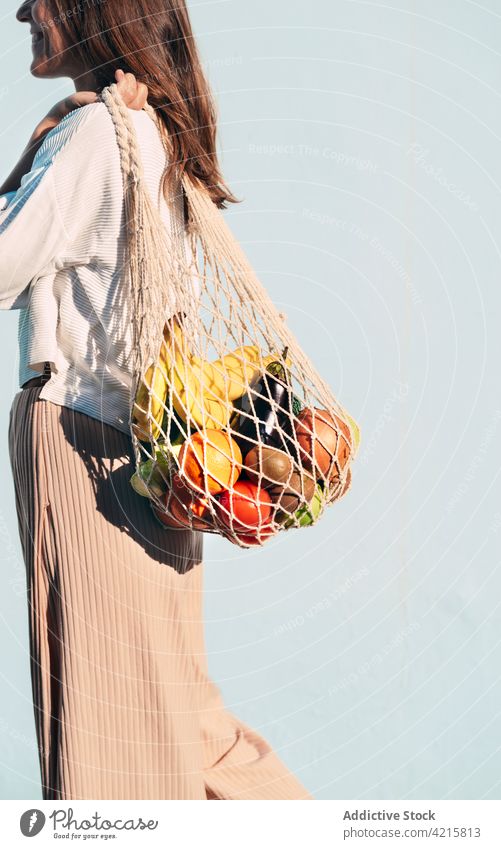 Cheerful woman with mesh bag full of ripe groceries grocery cotton food eco friendly zero waste fruit vegetable female smile cheerful content healthy food