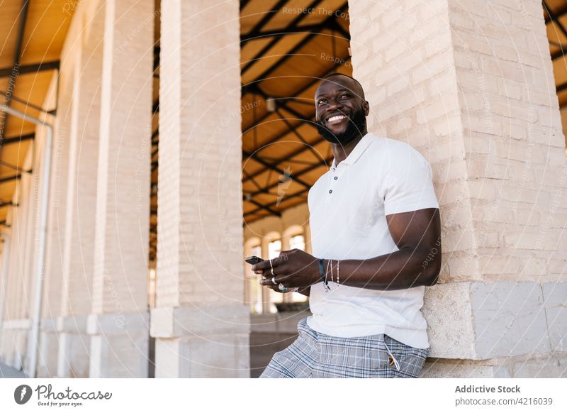 Smiling black man in rings browsing on smartphone cheerful style accessory using gadget device individuality t shirt bracelet smile content confident friendly