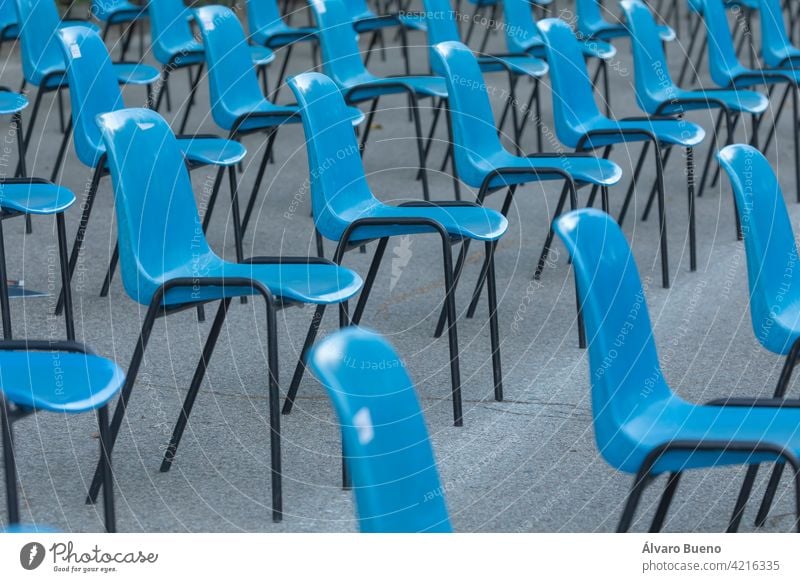 Rows and columns of nondescript blue plastic chairs, consecutive, arranged in a line, at similar intervals of space, facing the same place. Retiro Park, Madrid, Spain.