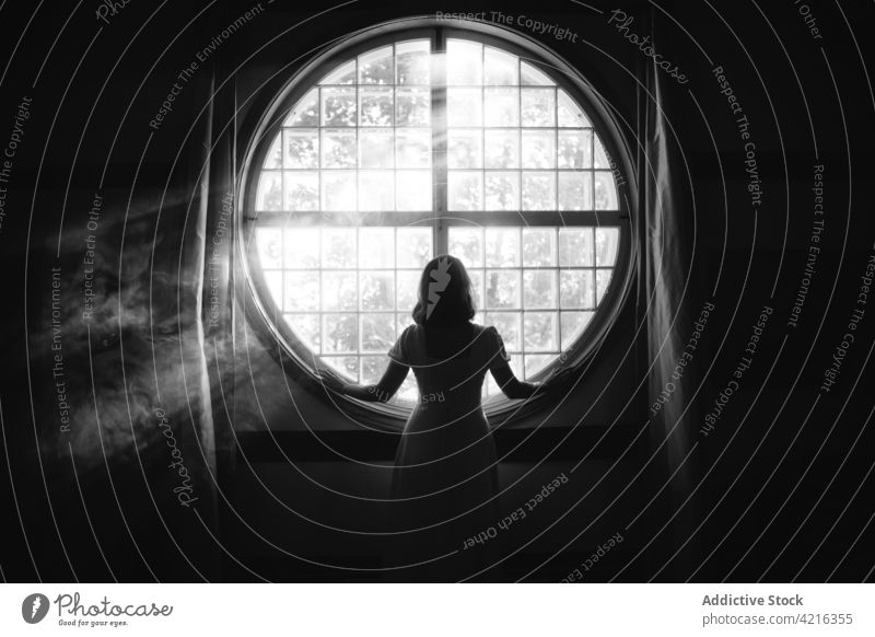 Anonymous woman looking out window at home in sunshine look out solitude gentle magic tender feminine house romantic idyllic sunbeam geometry air sunlight