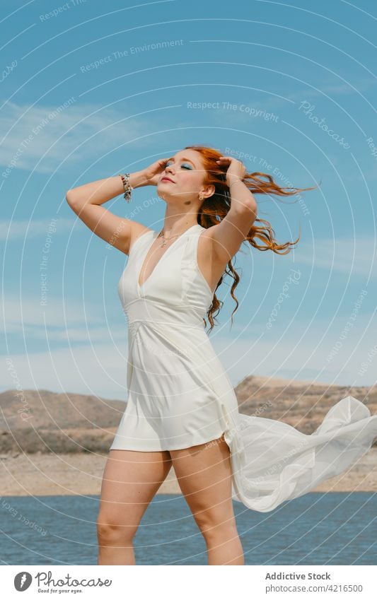 Feminine woman with flying hair against lake in summer eyes closed feminine dreamy romantic gentle allure portrait cloudy blue sky river flying dress