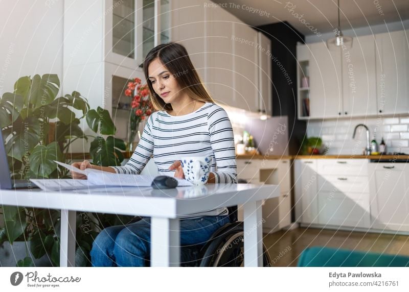 Woman in wheelchair reading documents at her desk at home domestic life disability disabled confidence woman independent indoors house people young adult casual