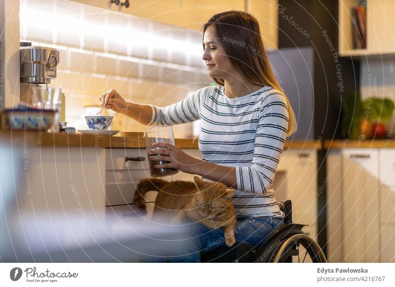 Disabled young woman in kitchen with cat on her lap wheelchair domestic life disability disabled confidence independent indoors home house people adult casual