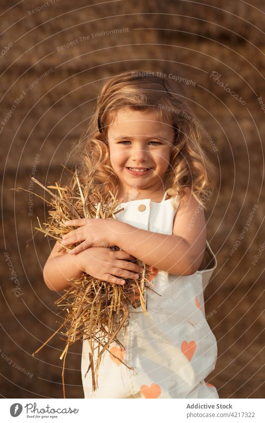 Cute girl playing with straw in field bale hay having fun countryside cheerful child childhood cute adorable kid nature overall idyllic little happy joy rural