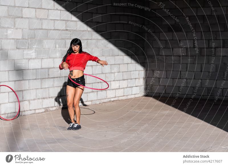 Dancer spinning hula hoop on pavement dancer active fit tattoo woman twirl movement choreography shadow body confident sportswear sneakers equipment asphalt