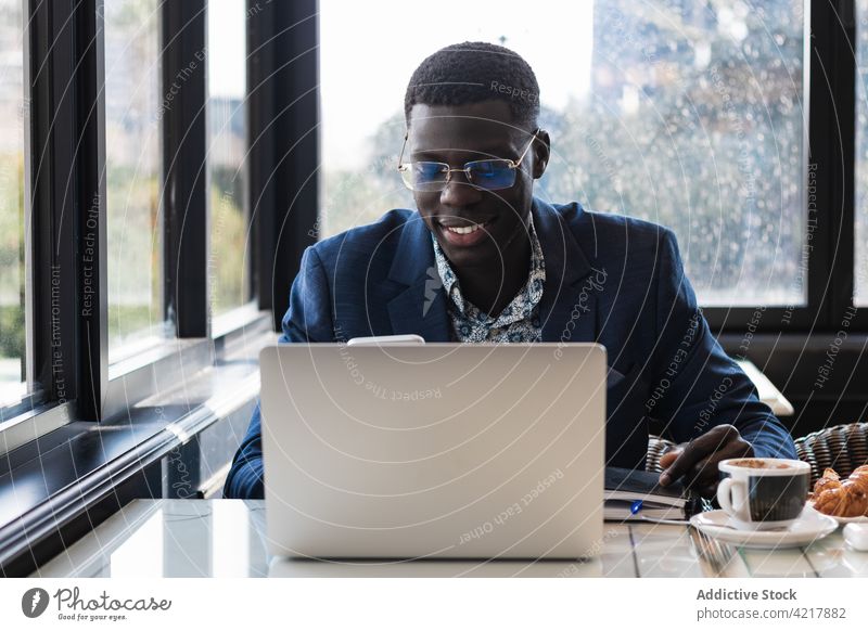 Stylish ethnic executive with smartphone and laptop in cafe work chatting well dressed breakfast man using gadget device cellphone watching eyeglasses