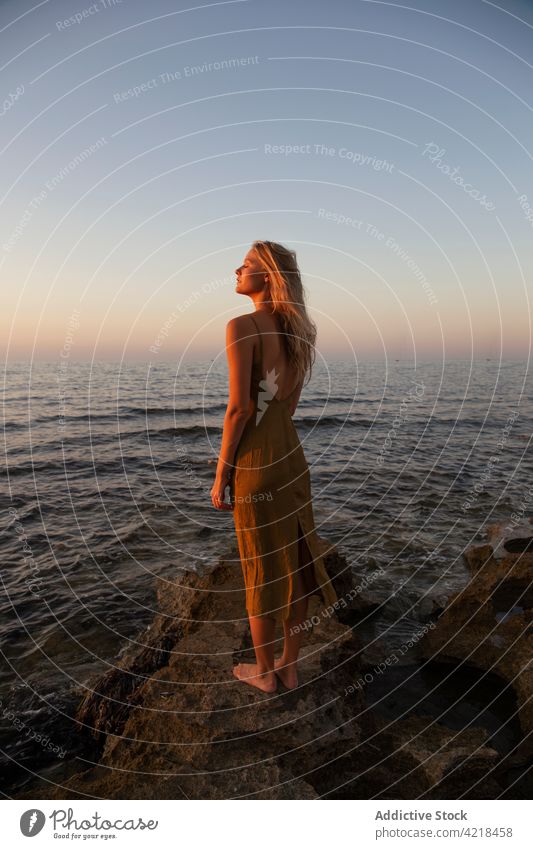 Peaceful female standing on rocky coast in evening woman shore sea nature environment sunset holiday carefree harmony peaceful vacation wave sundown seashore