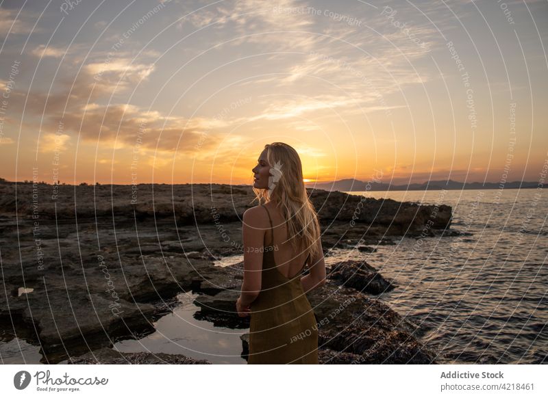 Peaceful female standing on rocky coast in evening woman shore sea nature environment sunset holiday carefree harmony peaceful vacation wave sundown seashore