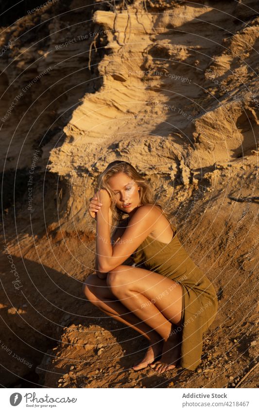 Young woman sitting on sandy ground in evening nature slope peaceful posture carefree harmony natural tranquil female serene blond vegetate recreation young